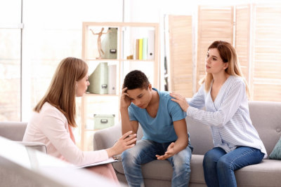 Young female psychologist working with teenage boy and his mother in office