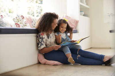  Mother sitting on the floor reading a book with her daughter