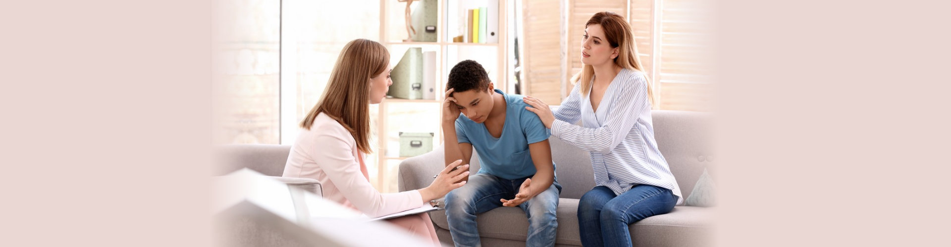 Young female psychologist working with teenage boy and his mother in office