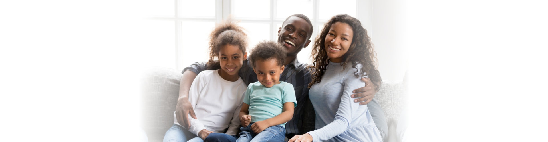 Portrait of happy large African American family at home sitting on couch together, smiling father embracing attractive wife and preschooler daughter, toddler son sitting on father knees look at camera